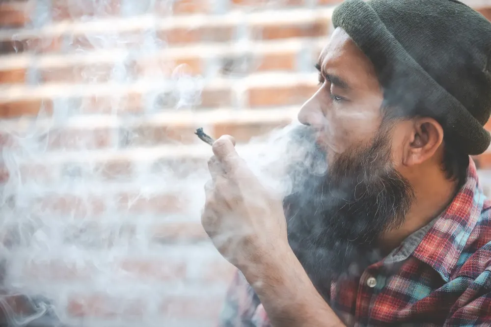 Man smoking a marijuana joint in front of a brick wall